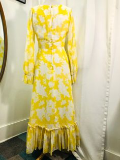 "Sunshine yellow and white floral print maxi dress from the Seventies! Dress has a slightly lower Empire waist with a band at the waist. A-line skirt with wide ruffle at the hem. Bodice has princess seams in the front. Long sleeves with elastic at the ruffled cuffs (elastic has been replaced). Back neck darts. Zipper closure in back with hook and eyes at the waist and neck. Lined. Cotton voile woven fabric. Manufactured by Jack Bryan. In good vintage condition with a small spot at the right side Yellow A-line Maxi Dress With Ruffles, Yellow Ruffle Hem Maxi Dress For Spring, Yellow Maxi Dress With Ruffle Hem, Yellow Ruffled Long Sleeve Maxi Dress, Yellow Long Sleeve Ruffled Maxi Dress, Yellow Long Sleeve Maxi Dress With Ruffles, Yellow Flowy A-line Maxi Dress, 1970s Style Yellow Spring Dress, Spring Retro Maxi Dress With Ruffles