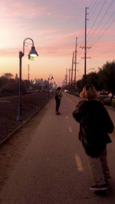 two people skateboarding down the street at sunset