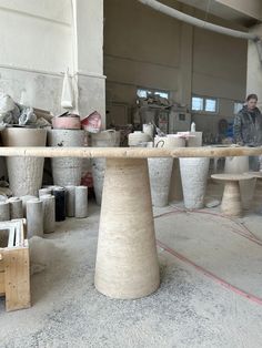 a man working in a pottery shop with several pots on the table and two stools behind him