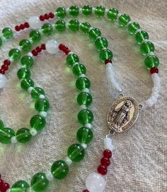 I have made and sold rosaries like this one for years but never thought to post one. This is the colors of the Mexican Flag. Main beads are green crystal. The Our Father and spacer beads are moonstone for the white.  The little red beads are also glass crystal. The middle medal is silver Our Lady of Guadalupe and the crucifix is also silver. This rosary will work as either a Mexican Flag or for a Christmas Rosary. It has a hanging length of 20 inches. The loop would be like putting on a 27 inch Green Beaded Spiritual Rosary Bracelet, Green Beaded Spiritual Rosary, Handmade Green Spiritual Rosary Bracelet, Green Spiritual Rosary Bracelet With Round Beads, Spiritual Green Rosary Bracelet With Round Beads, Green Beaded Rosary, Handmade Green Rosary, Green Beaded Rosary With Round Beads, Green Rosary With 8mm Beads