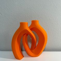 two orange vases sitting next to each other on a white counter top in front of a wall