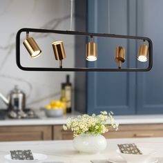 three lights are hanging over a kitchen counter top with plates and cups on the table