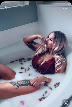 a woman sitting in a bathtub with rose petals on the floor and her legs