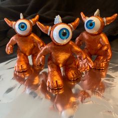 three little figurines with big eyes and horns on top of a shiny surface