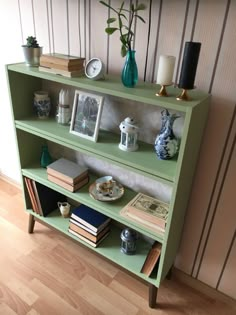 a green book shelf with books and vases on top