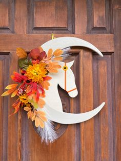 a wooden door with a white horse head decorated with fall leaves and flowers on it