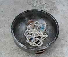 a metal bowl filled with lots of white beads and jewelry on top of a cement floor