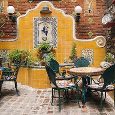 an outdoor dining area with yellow and white tiles on the wall, green chairs and tables