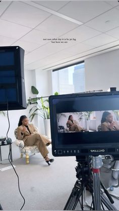 a woman sitting on a chair in front of a television screen with another person talking on the phone