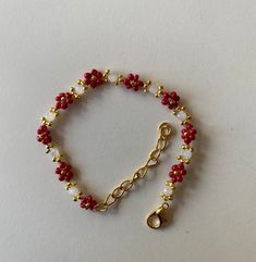 a red and white beaded bracelet with gold clasps on a white table top