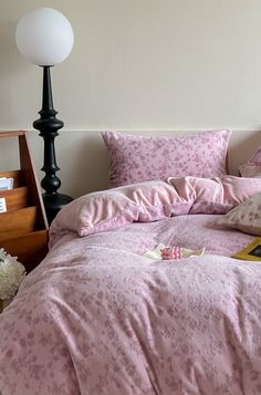 a bed with pink comforter and pillows on top of it next to a lamp