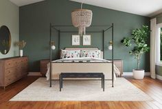 a bedroom with green walls and wooden flooring is pictured in this image, there is a four poster bed