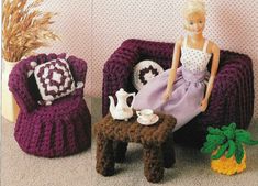 there is a doll sitting on a chair next to two crocheted chairs and a small table