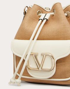 Valentino Garavani Locò synthetic raffia bucket bag with leather details and tone-on-tone enamelled VLogo Signature element. The bag can be worn on the shoulder/cross-body or handheld thanks to the removable handle and removable ribbon shoulder strap. - Platinum-finish hardware - Drawstring closure - Removable leather handle - Adjustable and removable ribbon shoulder strap - Cotton lining. Interior: slip pocket - Exterior pocket with magnetic closure - Shoulder strap drop length: min. 40 cm to m Valentino Straw Bag, Valentino Bucket Bag, Luxury Crochet Leather Bucket Bag, Luxury Basket-shaped Bucket Bag, Luxury Eco-friendly Bucket Bag With Braided Handles, Cole Haan, Leather Handle, Valentino Garavani, Online Boutique