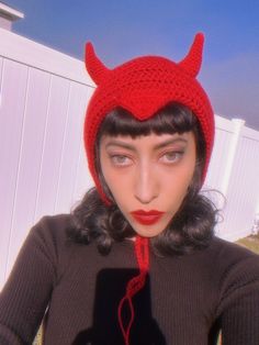 a woman wearing a red knitted devil hat with horns on it's head