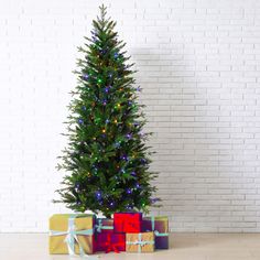 a christmas tree with presents under it in front of a brick wall and white bricks