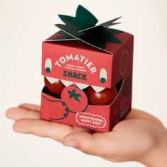 a hand holding an open box of tomatoes in the shape of a tomato with a bite taken out of it