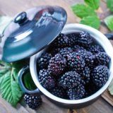 fresh blackberries in a bowl on a wooden table with leaves and an iron pot