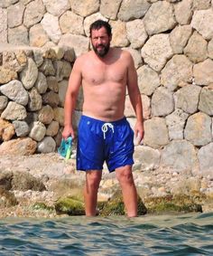 a man standing in the water next to a stone wall