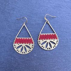 a pair of red and white beaded earrings on a blue surface with silver earwires