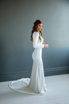 a woman in a long white dress is posing for the camera with her arms crossed