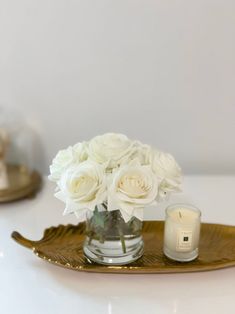 white roses in a glass vase on a gold tray next to a candle and some candles