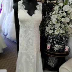 a white wedding dress on display in a bridal gown shop with flowers and other dresses