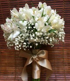 a vase filled with white flowers on top of a wooden table next to a bamboo wall