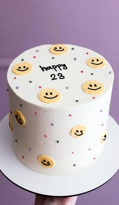 a hand holding a white cake with smiley faces on it and the words happy 29