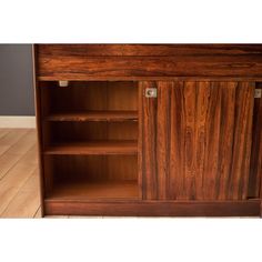 a wooden cabinet with two doors and shelves on the bottom, in front of a wood floor