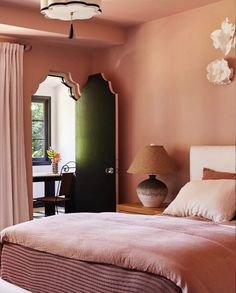 a bedroom with pink walls and white bedding in front of a doorway that leads to a dining room