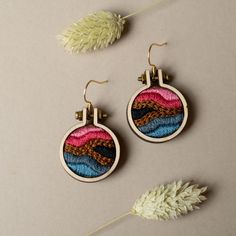 two pairs of earrings with colorful thread work on them, sitting next to each other