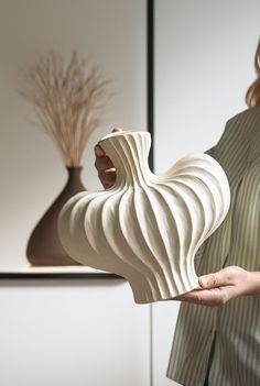 a woman holding a white vase in her right hand and a plant on the other