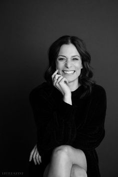 a black and white photo of a smiling woman with her hand on her chin, looking at the camera