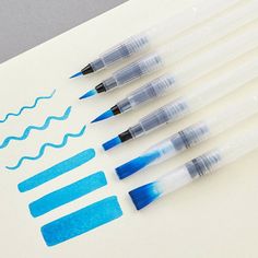 five pens are lined up on top of a piece of paper with some blue ink