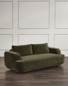 a green couch sitting on top of a hard wood floor next to a white wall