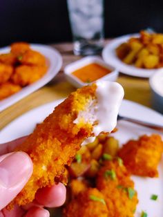 a person holding up a piece of fried food on a plate with other plates in the background