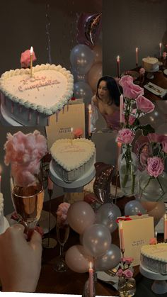 a woman sitting in front of a table filled with cakes and balloons, candles and flowers