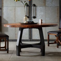 a wooden table with two chairs and a vase on top of it, in front of a concrete wall