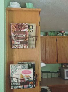 a book shelf with books and magazines on it next to a microwave oven in a kitchen