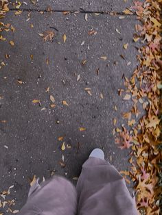 the person is standing on the sidewalk with their feet in the air and there are leaves all over the ground