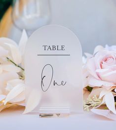 a table name sign sitting on top of a table next to some flowers and wine glasses