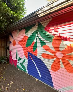 a garage door painted with colorful flowers and leaves on it's side in front of a tree