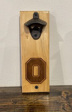 a bottle opener with the letter o on it sitting on top of a wooden table