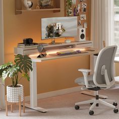 a white desk with a computer monitor and keyboard on it next to a potted plant