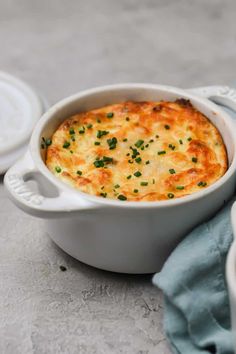 a white casserole dish with cheese and parsley on top, next to two plates