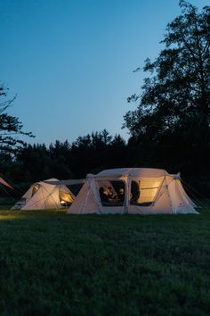 two tents are lit up at night in the grass