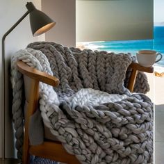 a large chunky blanket sitting on top of a wooden chair next to a lamp