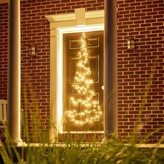 a lighted christmas tree sitting in front of a door on a brick house's porch