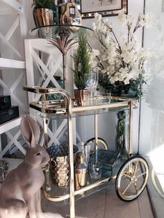 a rabbit sitting on the floor next to a cart with flowers and glasses in it